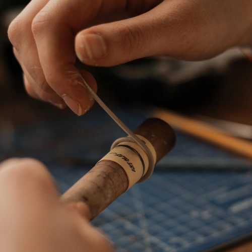 Close-up of hands skillfully wrapping a cigar in a studio setting, showcasing the art of cigar preparation.